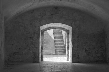 Gray scale image of arched exit from an old fortress room, that frames a staircases