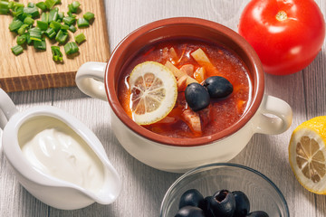 Soup saltwort with meat, potatoes, tomatoes, lemon, black olives and sour cream in ceramic soup bowl