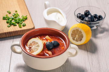 Soup saltwort with meat, potatoes, tomatoes, lemon, black olives and sour cream in ceramic soup bowl