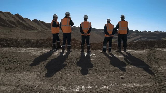 Panorama shot of a group of workers in overalls actively speaking on board a bauxite quarry.