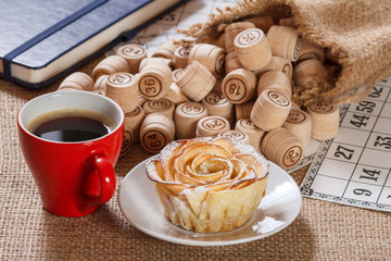 Board game lotto on sackcloth. Wooden lotto barrels in bag and game cards with notebook, cup of coffee and homemade cookie on plate