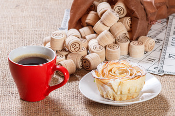 Board game lotto on sackcloth. Wooden lotto barrels in bag and game cards with cup of coffee and homemade cookie on plate