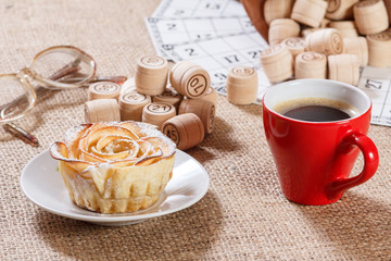 Board game lotto on sackcloth. Wooden lotto barrels and game cards with cup of coffee and homemade cookie on plate