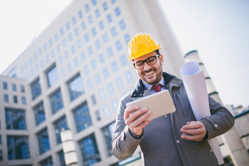 Architect in protective helmet using digital tablet in front of office building