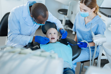Coordinated work. Pleasant male dentist carrying out an examination of her little patients oral...
