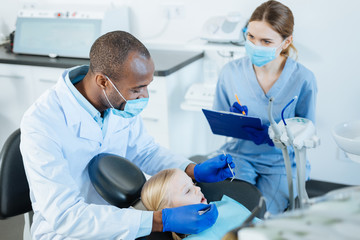 Vital notes. Charming young female nurse making notes of dentists observations while he carrying out a thorough checkup of a little girls oral cavity