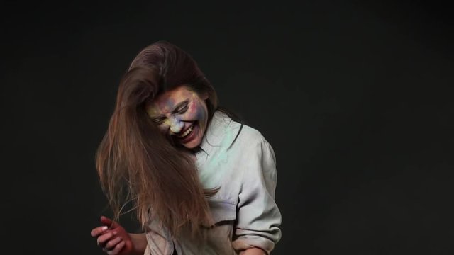 Portrait of beautiful woman dancing and being thrown with colorful splashes of paints on holi asian party, isolated over dark gray background slow motion. Indian culture and tradition