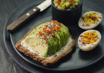 Wholegrain Toast with avocado and creamy cheese,and boiled egg,serves with fresh lemon and on dark plate. 