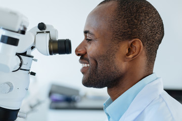 State-of-the-art device. The side view of a pleasant upbeat male dentist smiling widely while using...
