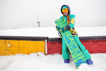 Beautiful happy young snowboarder sitting with her snowboard.
