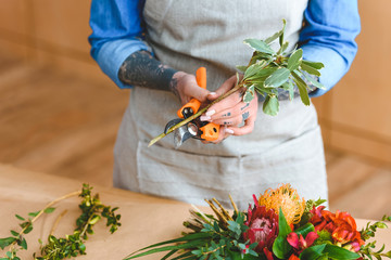 mid section of young florist in apron cutting plants at workplace - Powered by Adobe
