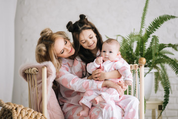 Portrait of mother with two daughters in the white room in the same pink pajamas, family look