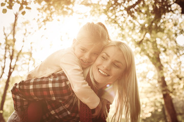 Fototapeta premium Smiling mother carrying her daughter on piggyback and enjoying in nature.