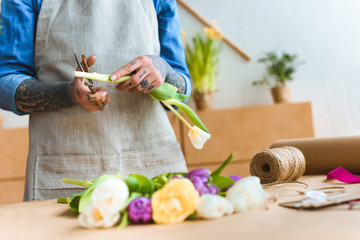 cropped shot of florist in apron cutting tulip flower