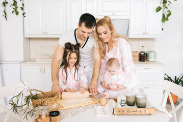 Obraz na płótnie Canvas Happy loving family are preparing bakery together. Mother father and two daughter girl are cooking cookies and having fun in the kitchen. Homemade food and little helper.