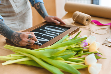 cropped shot of florist writing word open on board in flower shop