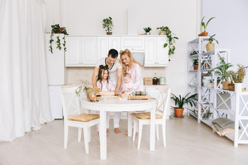 Happy loving family are preparing bakery together. Mother father  and two daughter girl are cooking cookies and having fun in the kitchen. Homemade food and little helper.
