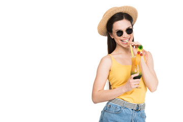 smiling girl in sunglasses and hat drinking cocktail, isolated on white