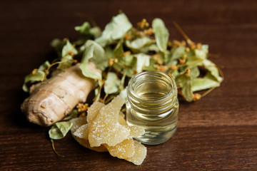 A horizontal photo of light yellow shooter alcoholic drink, garnished with fresh and sugared ginger, dried lime-blossoms.