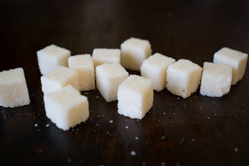 A few cubes of white crystalline refined sugar on a dark old background