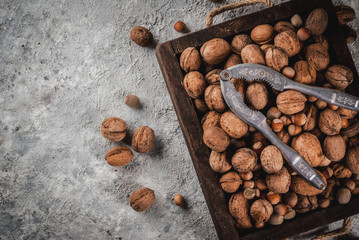 Various nuts and nutcracker in wooden box. On rustic grey stone table, copy space