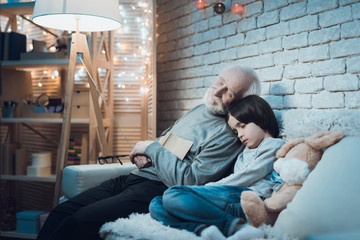 Grandfather and grandson are sleeping sitting at night at home.