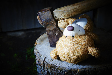 Toy teddy bear lying on a wooden log killed by an ax