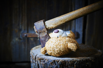 Toy teddy bear lying on a wooden log killed by an ax