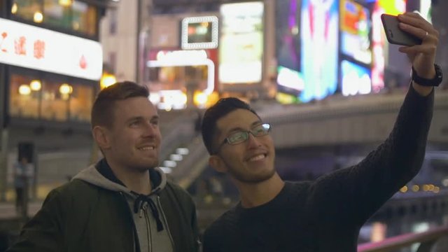 International friends taking selfies in a Japanese city at night, on holiday.