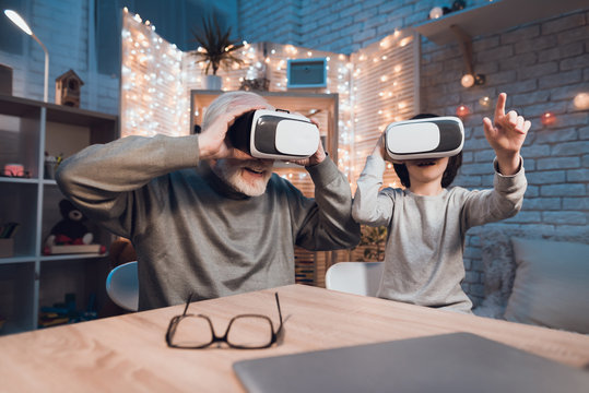 Grandfather and grandson are using virtual reality at night at home.