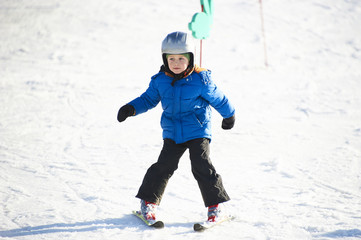 Fototapeta na wymiar Child boy skiing in winter mountains. Active kid with safety helmet and goggles. Ski race for young children. Winter sport for family. Kids ski lesson in school. Young skier racing in snow