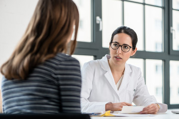 Female physician listening to her patient during consultation while sitting down in the office of a...