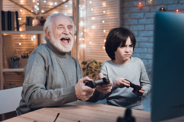 Grandfather and grandson are playing video games on computer at night at home.