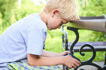 Child boy sitting on a bench and playing game with smartphone 