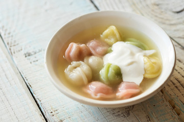 multi-colored dumplings with sour cream in a white plate on wooden background