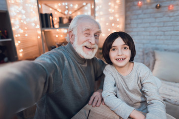 Grandfather and grandson are taking selfie at night at home.