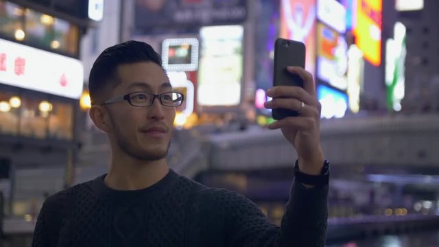 Asian Man taking selfies in a Japanese city at night, on holiday.