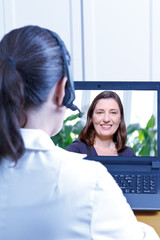 Physician with headset in front of her laptop during an online consultation with a female patient,...