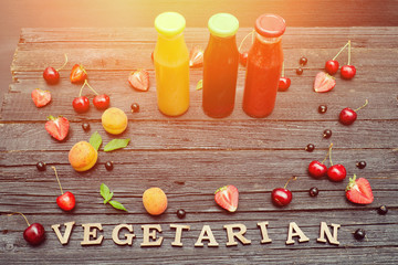 Three bottles with juice, fruit and inscription Vegetarian on black wooden background. Food concept
