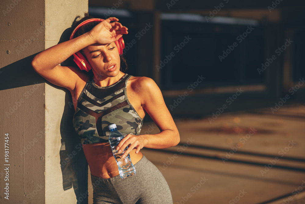 Wall mural Young woman resting and drinking water after jogging