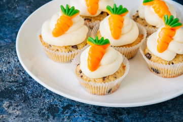 Vanilla cupcakes with chocolate chips and cream cheese frosting decorated with carrot marmalade in a plate on a blue stone background.