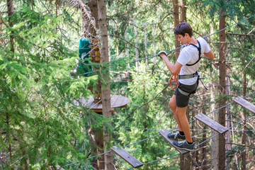Teenager boy having fun on high ropes course, adventure, park, climbing trees in a forest in summer