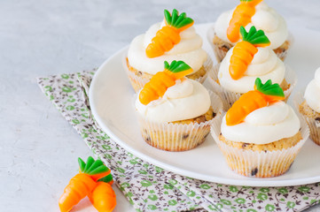 Vanilla cupcakes with chocolate chips and cream cheese frosting decorated with carrot marmalade in a plate on a white stone background.
