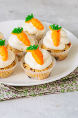 Vanilla cupcakes with chocolate chips and cream cheese frosting decorated with carrot marmalade in a plate on a white stone background.