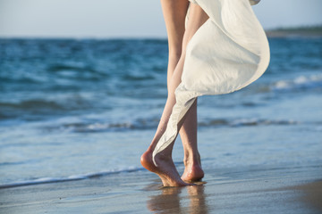 Beautiful woman in a white dress walking along the edge of the beach during a sunset. Horizon line