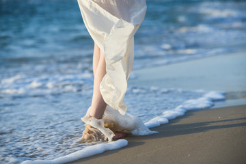 Beautiful woman in a white dress walking along the edge of the beach during a sunset. Horizon line