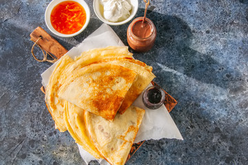 Delicious crepes (blinis) with assorted sauces on a wooden board on a blue stone background. Top...