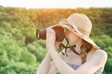 Girl in hat takes pictures against the background of green forest. Side view