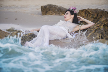 Beautiful mermaid having rest on rocks in wavy sea. Fantasy and myth. Woman in white dress lying in the sea.