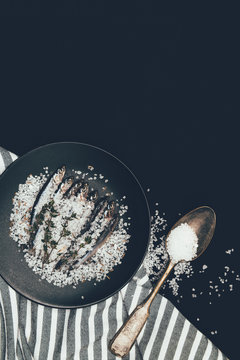 Frying pan with salted pile of fish, rosemary , spoon and towel isolated on black